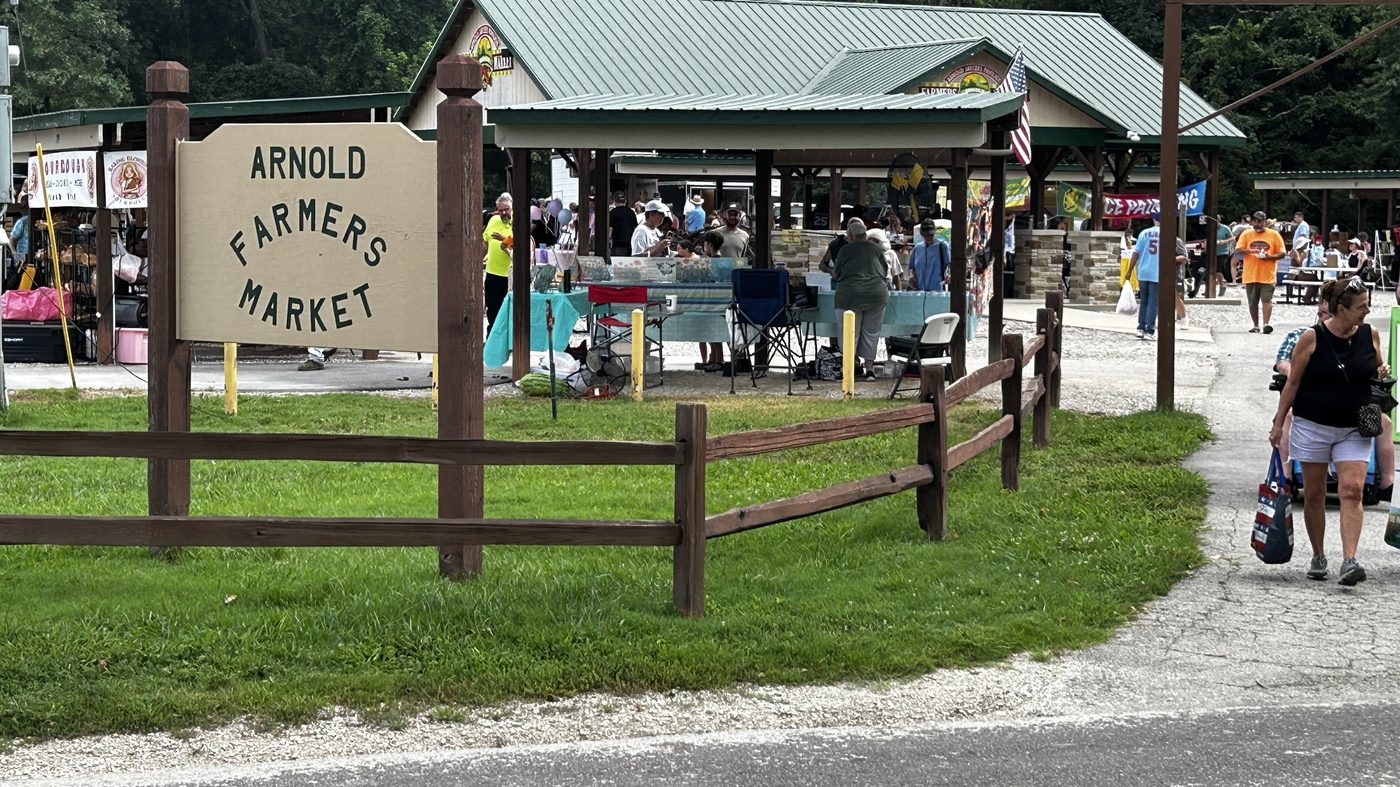 The Arnold Farmers Market entrance sign, with shoppers under the pavilion behind it