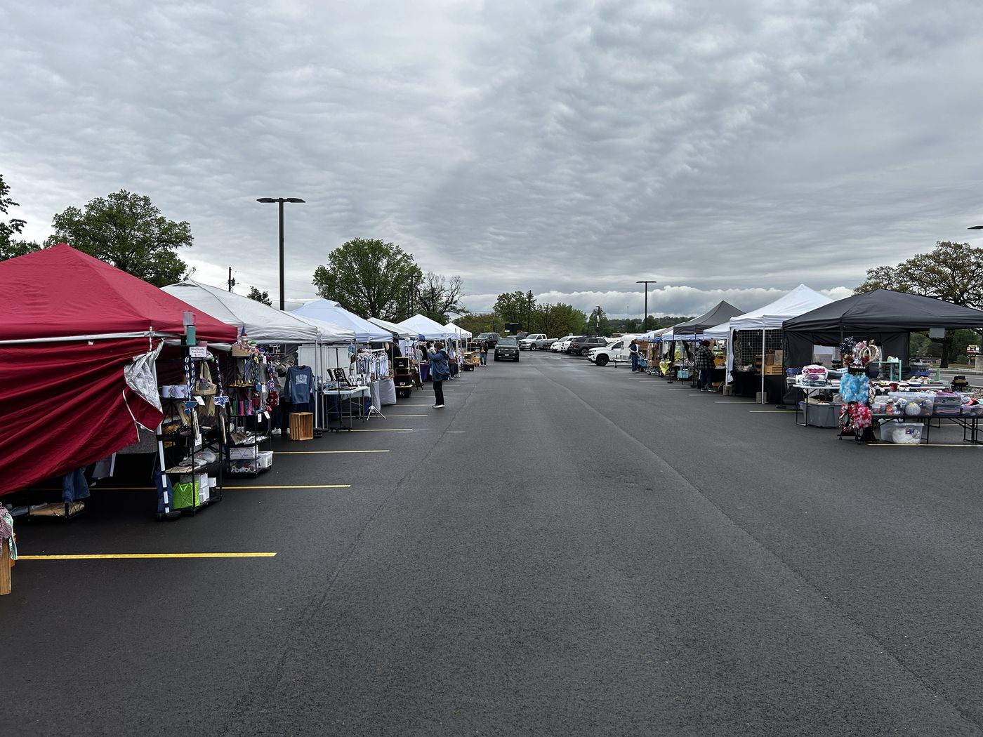 Two rows of vendor tents facing each other down a school parking lot aisle under a wide cloudy sky