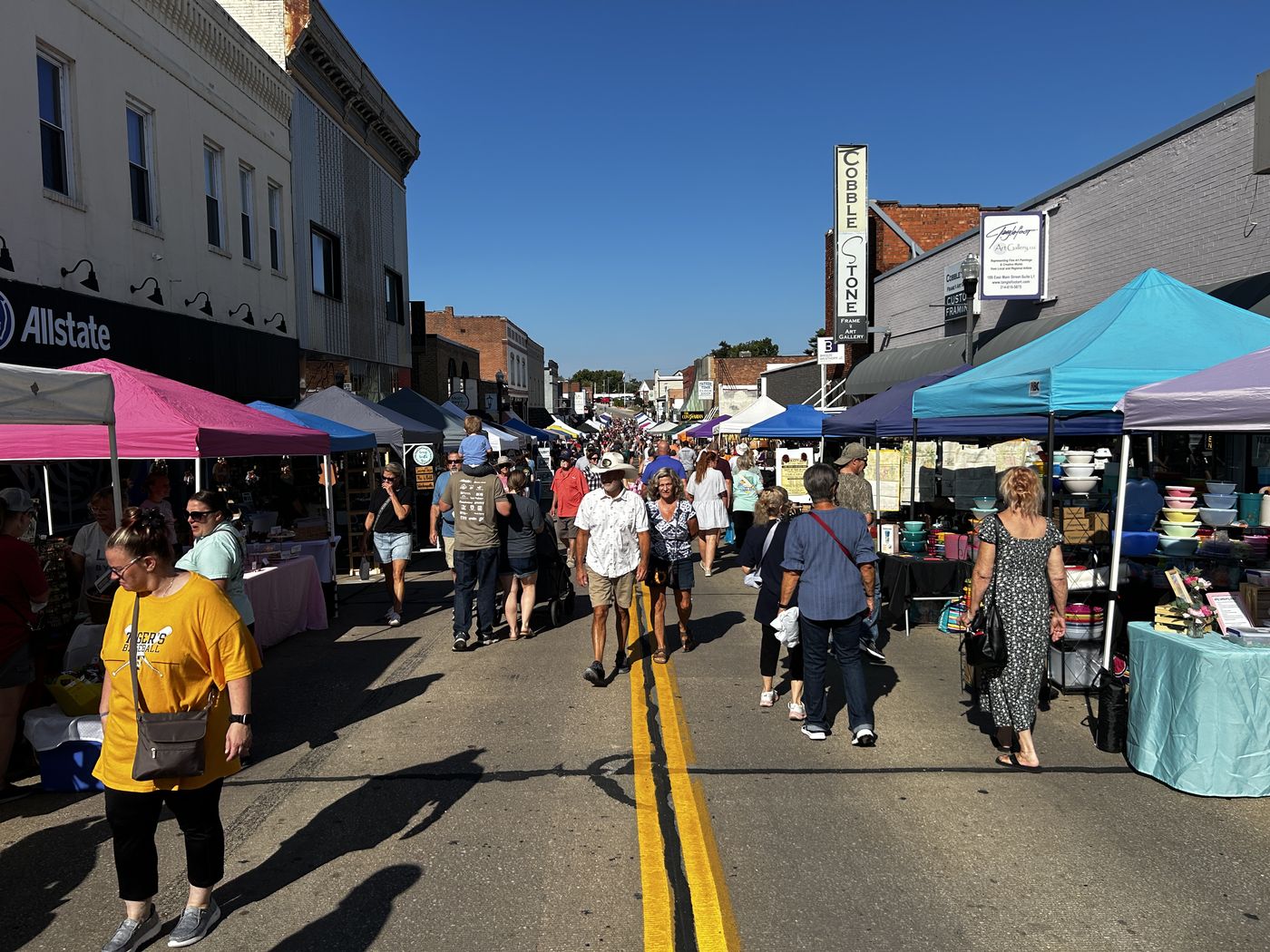 Main Street closed to traffic with vendor tents down both sides, shoppers filling the middle of the block under a clear sky